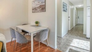 A modern dining area with a white table and two grey chairs, a small potted plant, and a painting on the wall. - Fort Charm (Fort Saskatchewan)