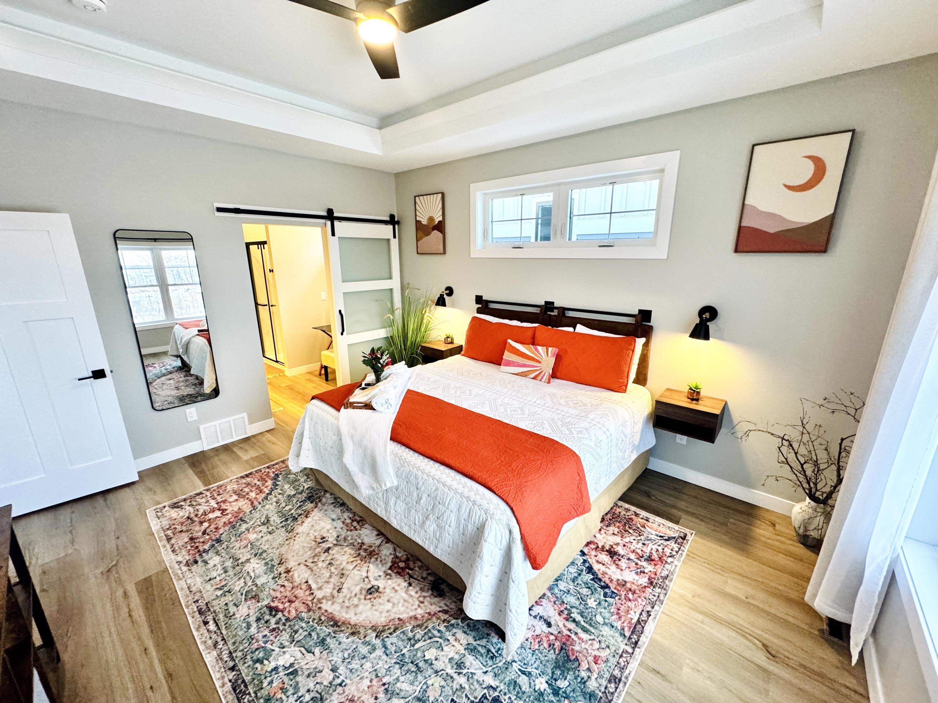 A bedroom with a bed, bedside tables, a mirror, a window, and a door.