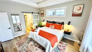 A bedroom with a bed, bedside tables, a mirror, a window, and a door.