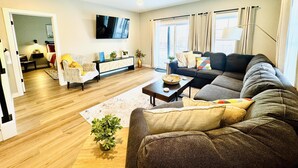 Een woonkamer met een bank, fauteuil, salontafel en een televisie aan de muur.
