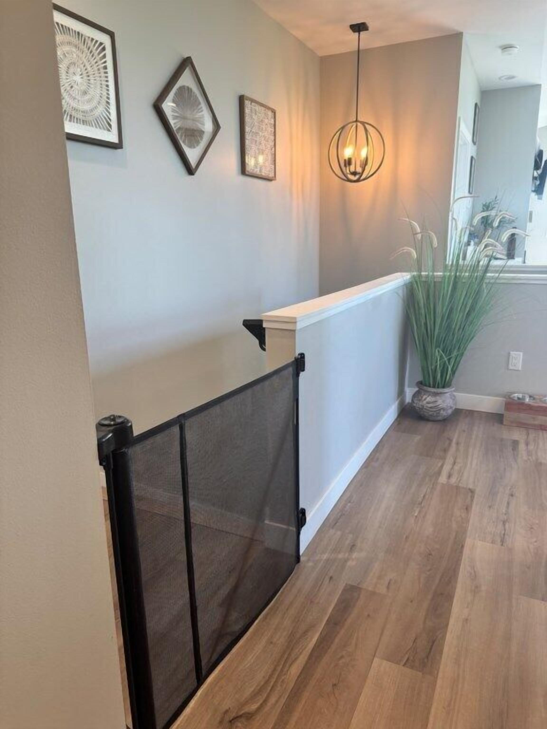 A hallway with a wooden floor, a white railing, and a hanging light fixture.