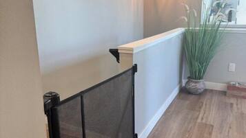 A hallway with a wooden floor, a white railing, and a hanging light fixture.