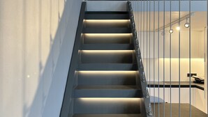Un escalier moderne doté d’un éclairage intégré, menant à une chambre à coucher équipée d’un lit et d’un espace bureau.