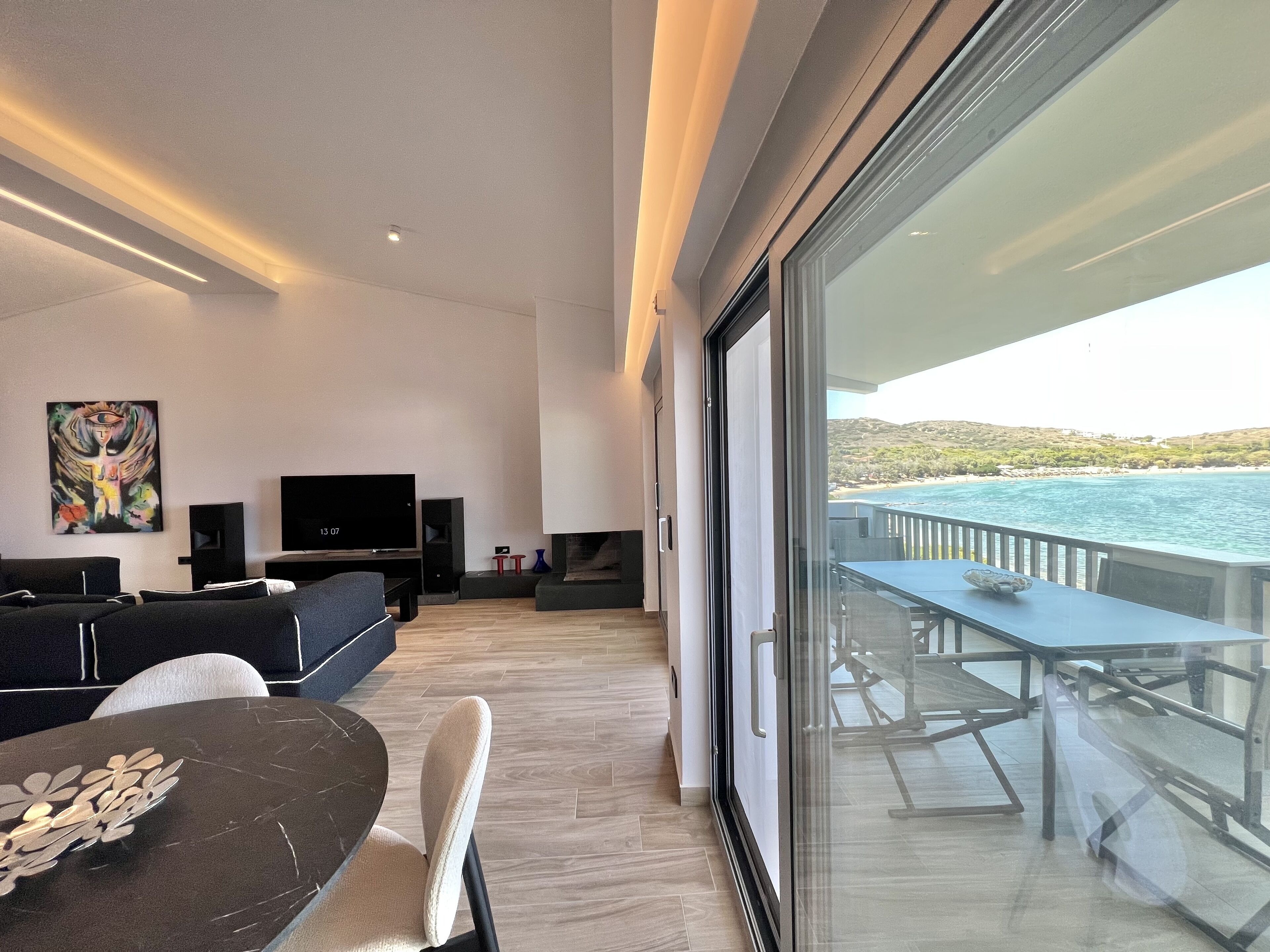 Una sala de estar moderna con un televisor grande, asientos cómodos y un balcón con vistas al mar.