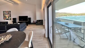 Un salon moderne doté d’un grand téléviseur, de sièges confortables et d’un balcon offrant une vue sur la mer.