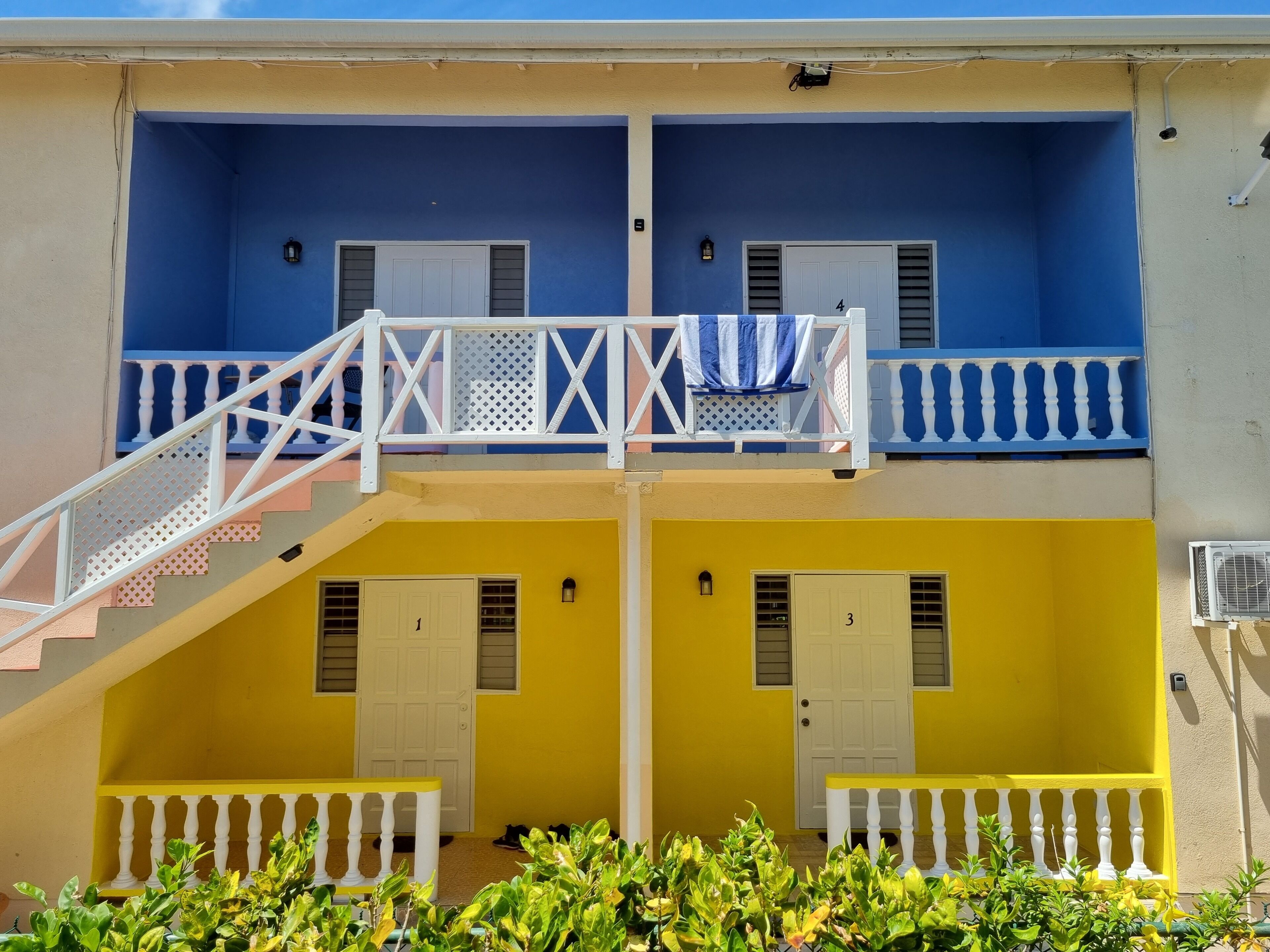 A two-story building with balconies, white railings, and a staircase leading to the upper floor.