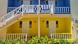 Un edificio de dos pisos con balcones, barandillas blancas y una escalera que conduce al piso superior.