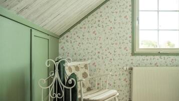 Une pièce avec un plafond en pente, un radiateur, un papier peint à motifs floraux et une fenêtre.