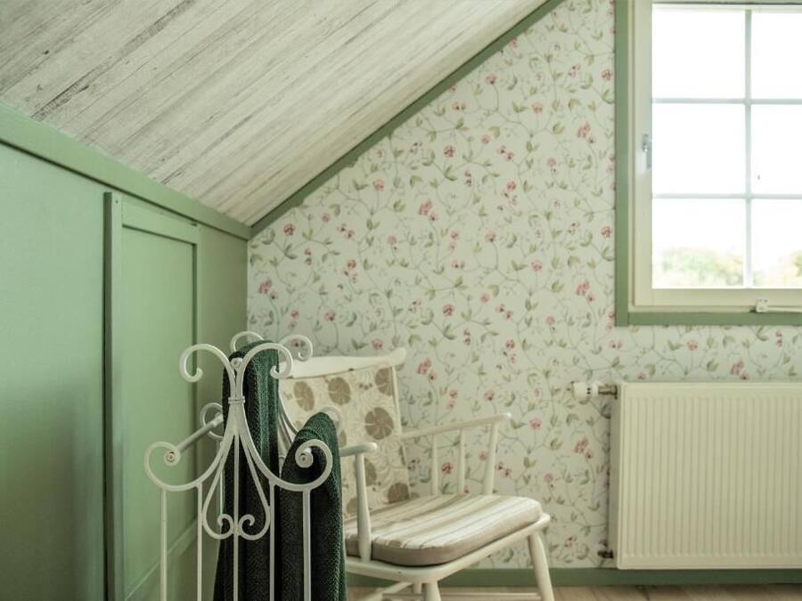 Une pièce avec un plafond en pente, un radiateur, un papier peint à motifs floraux et une fenêtre.