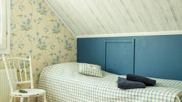 A bedroom with a checkered bedspread, a blue headboard, a white chair, and floral wallpaper.