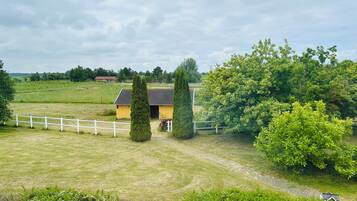 A rural landscape with a yellow building, white fence, and green trees.