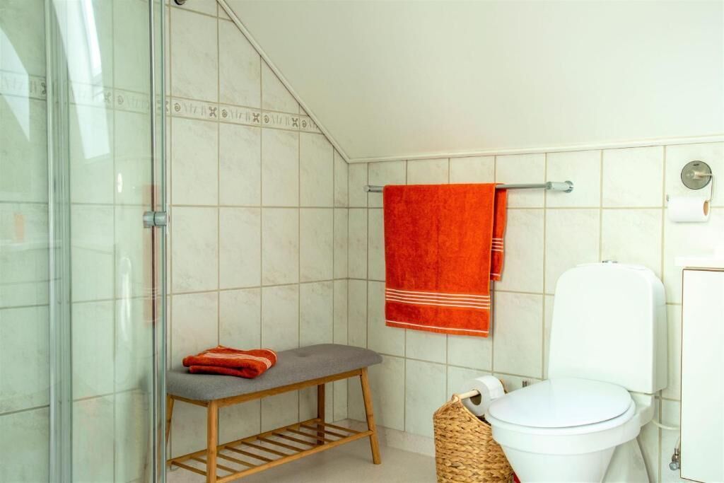 Et badeværelse med en brusekabine i glas, et hvidt toilet, en håndklæderække med et rødt håndklæde og en fletkurv.