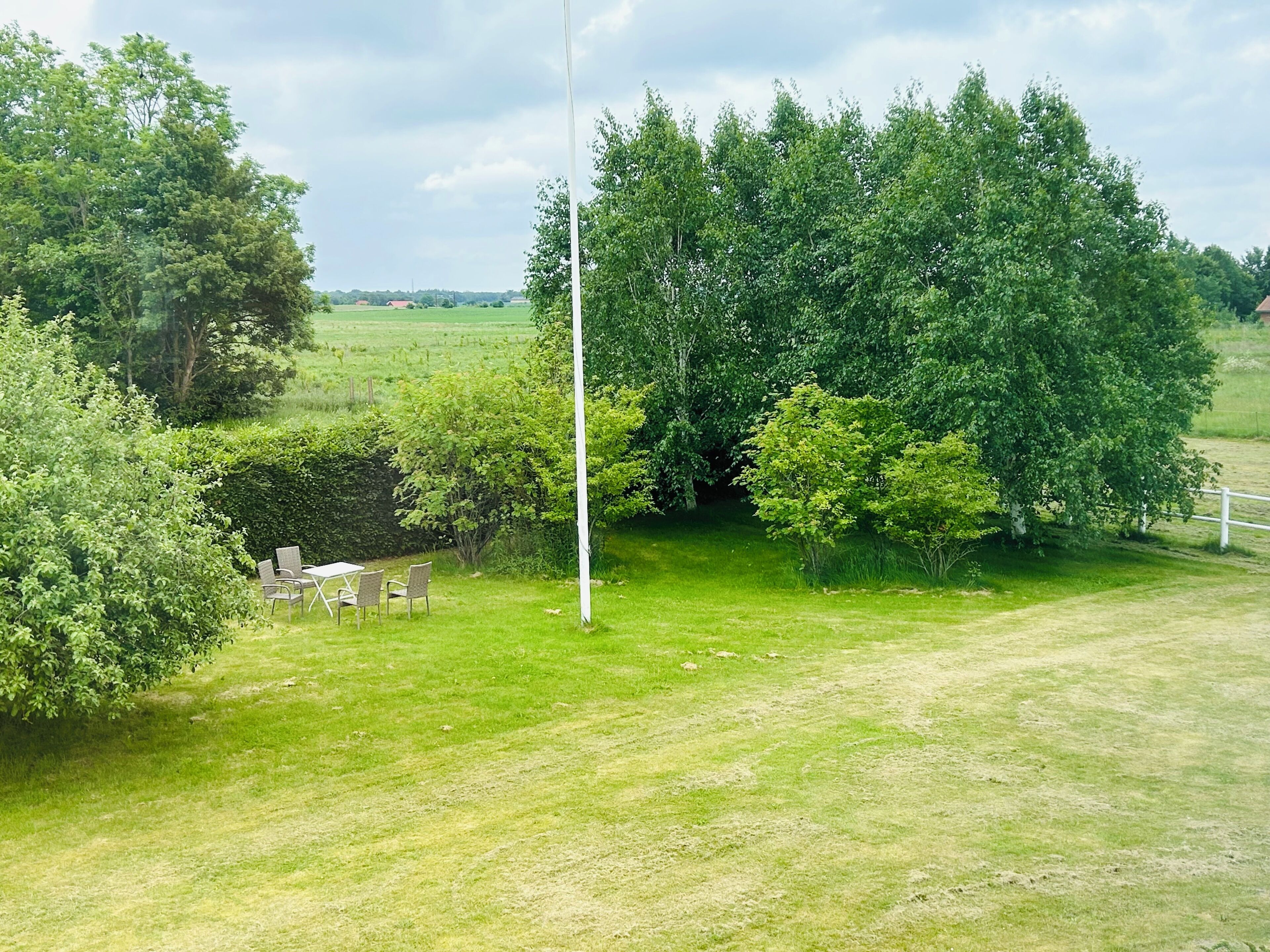 A grassy outdoor area with a white pole, a hedge, and a table with chairs.