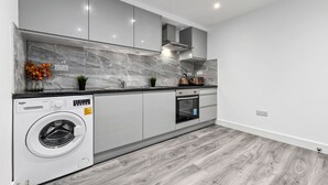 A modern kitchen with a built-in washing machine, grey marble backsplash, and wooden flooring. - Luxury Ensuite Room in Finsbury Pak London N19 (London)