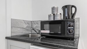 A modern kitchen with a black microwave, a coffee maker, and a tea kettle on the countertop. - Luxury Ensuite Room in Finsbury Pak London N19 (London)