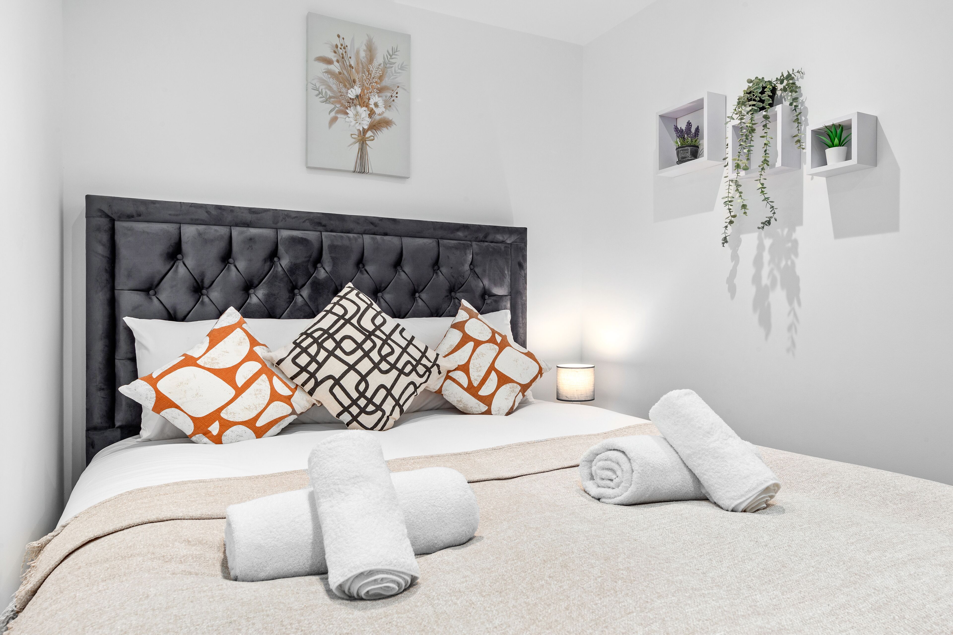 A modern bedroom with a tufted headboard, patterned pillows, a neutral-toned bedspread, and neatly folded towels.