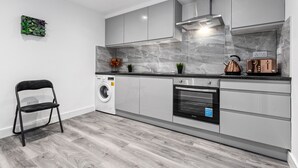 A modern kitchen with grey cabinets, a built-in oven, a washing machine, and a kettle. - Charming Ensuite Room in Finsbury Park London N19 (London)