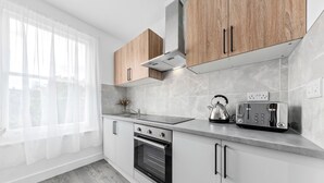 A modern kitchen with white cabinets, a built-in oven, a toaster, and a window with sheer curtains. - Charming Ensuite Room in Finsbury Park London N19 (London)