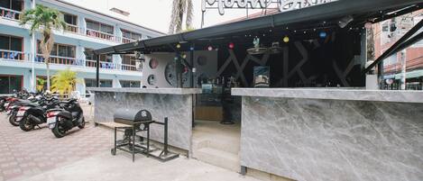 A restaurant with a marble counter and outdoor seating, surrounded by parked scooters and a multi-story building in the background.