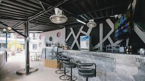 A modern bar area with a marble counter, black bar stools, and a large TV screen displaying various channels. - O'shop Residence Patong Beach (Patong)