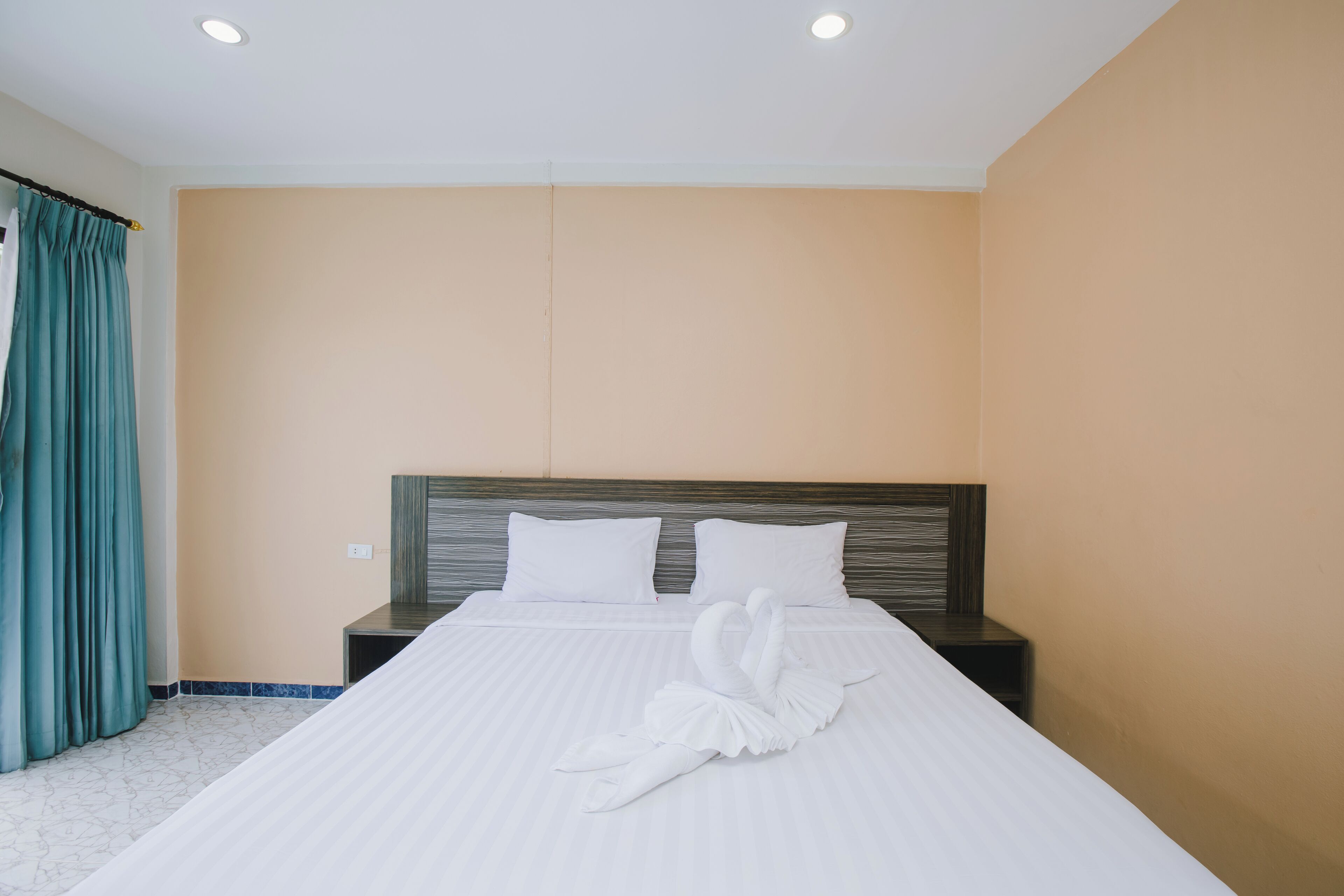 Hotellihuone, jossa on suuri sänky, kaksi tyynyä, sängynpääty ja yöpöytä.