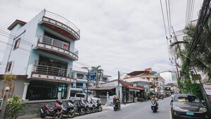 A street view with a row of parked motorcycles, a building with a balcony, and a signboard. - O'shop Residence Patong Beach (Patong)