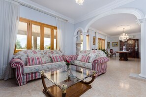Un ampio soggiorno con due divani, un tavolino in vetro e una zona pranzo illuminata da un lampadario.