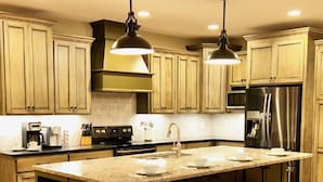 A kitchen with wooden cabinets, a central island with stools, stainless steel appliances, and pendant lighting. - Lake Martin, AL
43 min to Auburn University & Jordan-Hare Stadium (Dadeville)