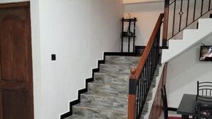 A staircase with a wooden handrail and black balusters, leading to a landing with a small table and a chair. - New 5 bed Room Villa (Piliyandala)
