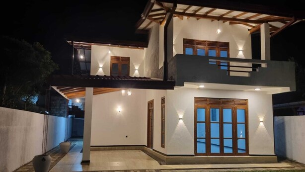 A two-story modern house with a covered patio, large windows, and exterior lighting. - New 5 bed Room Villa (Piliyandala)