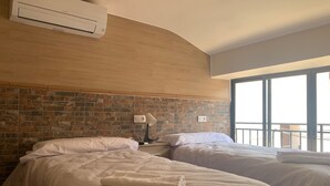 A hotel room with two beds, a brick-patterned headboard, a window with a balcony, and an air conditioning unit. - Hostal Valdeverdeja (Valdeverdeja)