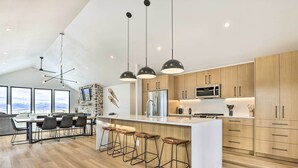 A modern kitchen with a central island, bar stools, and a dining area with a view. - New Modern Mountain Retreat with Level 2 EV Charger (Granby)