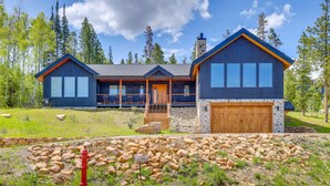 A modern two-story house with a stone foundation, large windows, and a wooden garage door. - New Modern Mountain Retreat with Level 2 EV Charger (Granby)