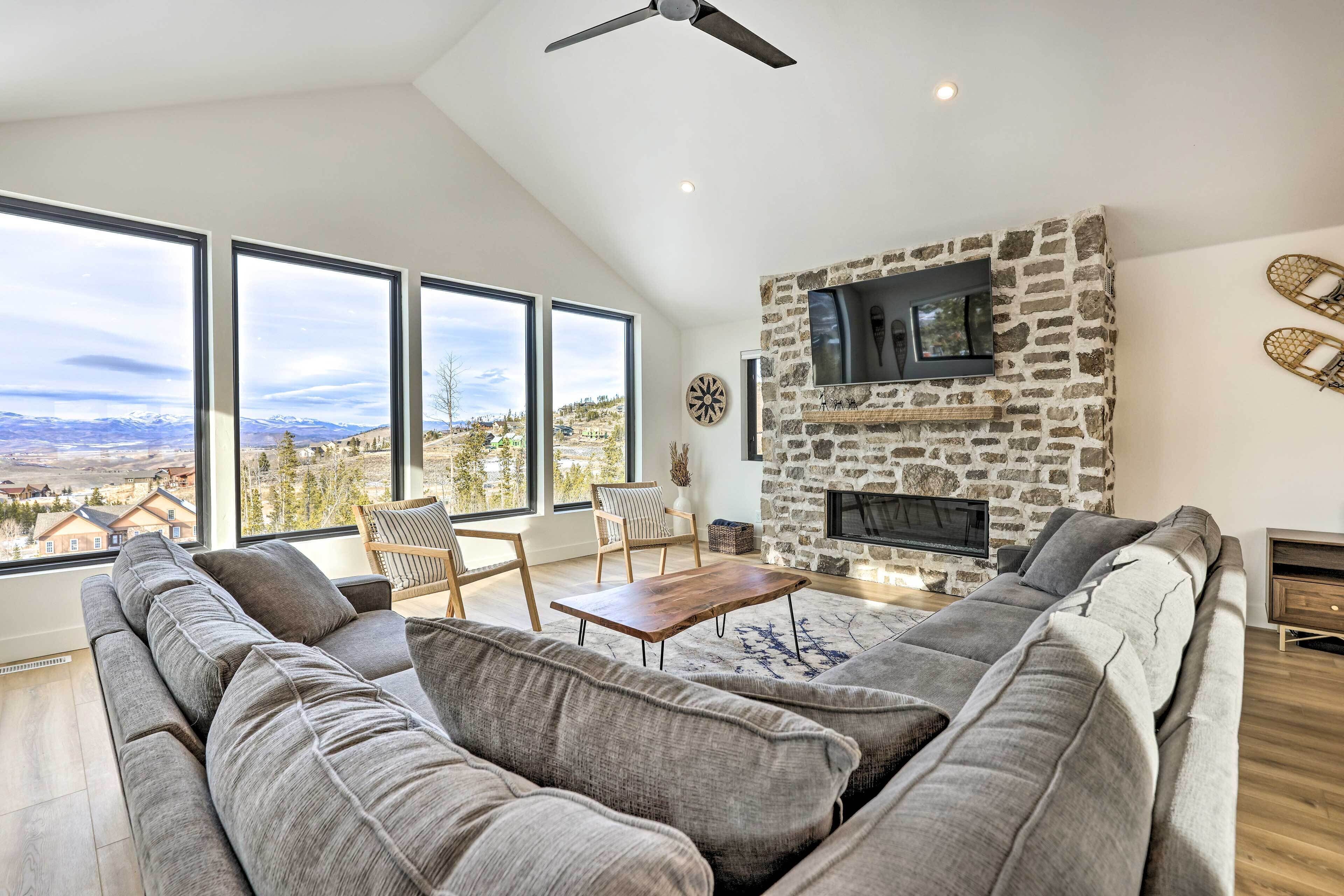A modern living room with a stone fireplace, large windows, and a view of the mountains.