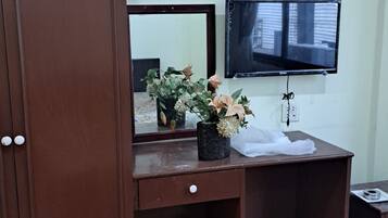 A room with a wooden desk, a television mounted on the wall, a wardrobe, and an air conditioning unit.