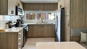 A modern kitchen with wooden cabinets, a built-in microwave, a refrigerator, and a large island with a sink.
