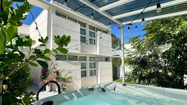 A hot tub area with a pergola overhead, surrounded by greenery and a modern building.