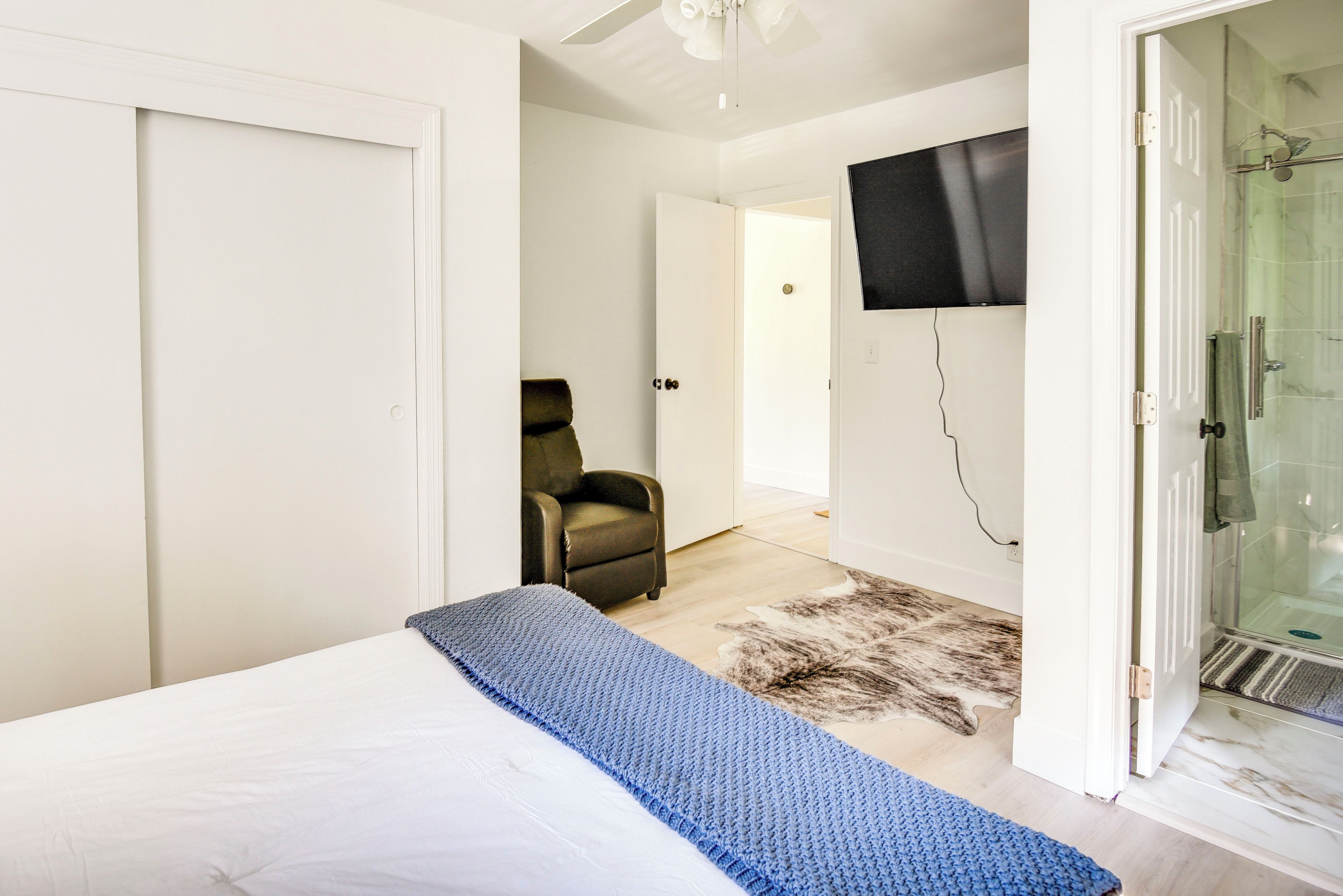 A bedroom with a bed, a chair, a television, and a shower area.
