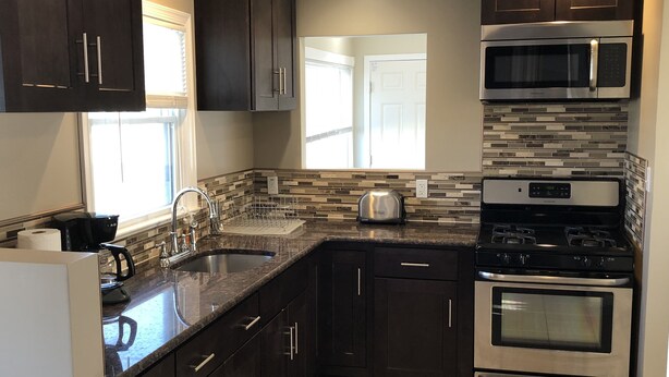 A modern kitchen with dark cabinets, a stainless steel microwave, a double oven, and a granite countertop. - Newly Renovated 2 Bedroom House (Seaside Heights)
