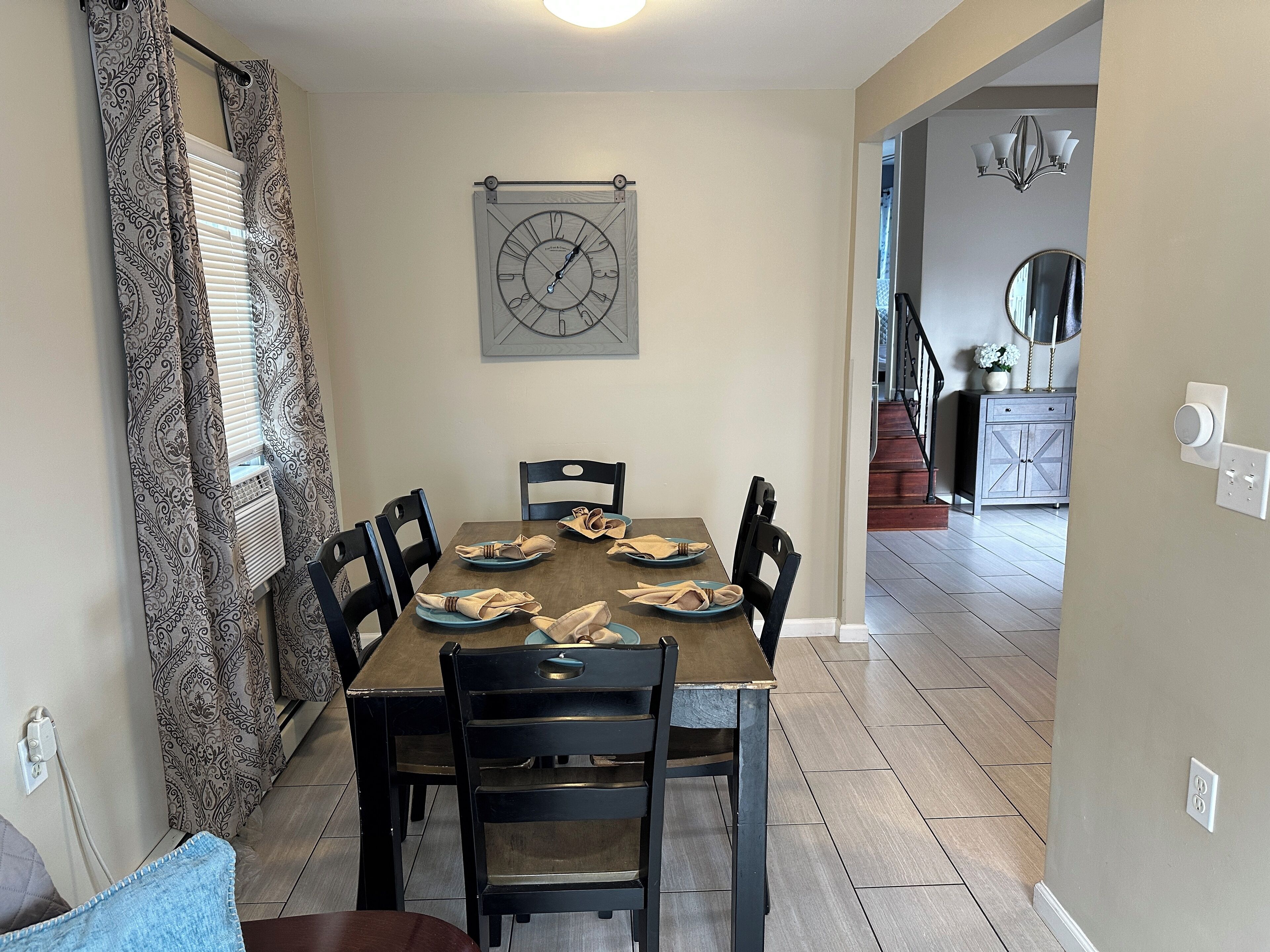 A dining area with a wooden table, black chairs, and a wall clock.