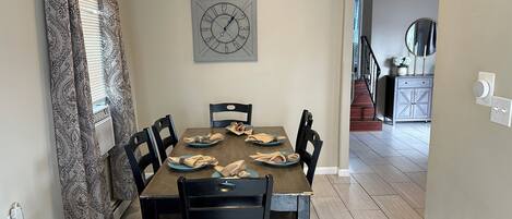 A dining area with a wooden table, black chairs, and a wall clock.