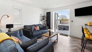 A modern living room with a sofa set, a coffee table, and a TV. - The Paddock - Lovely Cottage with Hot Tub (Penally)