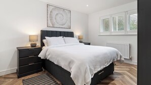 A modern bedroom with a large bed, two bedside tables, a wall-mounted artwork, and a window with blinds. - The Paddock - Lovely Cottage with Hot Tub (Penally)