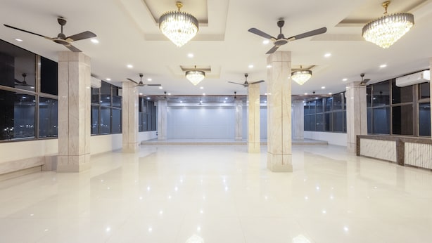 A spacious, well-lit room with marble columns, ceiling fans, and chandeliers. - Treebo Royal Palace, Zoo Road (Guwahati)