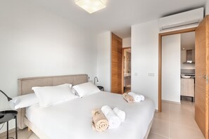 Ein Hotelzimmer mit Bett, Schreibtisch, Lampe und sichtbarem Badezimmer durch eine offene Tür, sowie einer Klimaanlage.