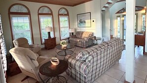 Un salon spacieux avec un plafond haut, de grandes fenêtres et un coin salon confortable avec un canapé et des fauteuils.