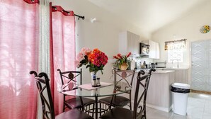 Een eethoek met een glazen tafel en stoelen, een vaas met bloemen, en een keuken op de achtergrond.