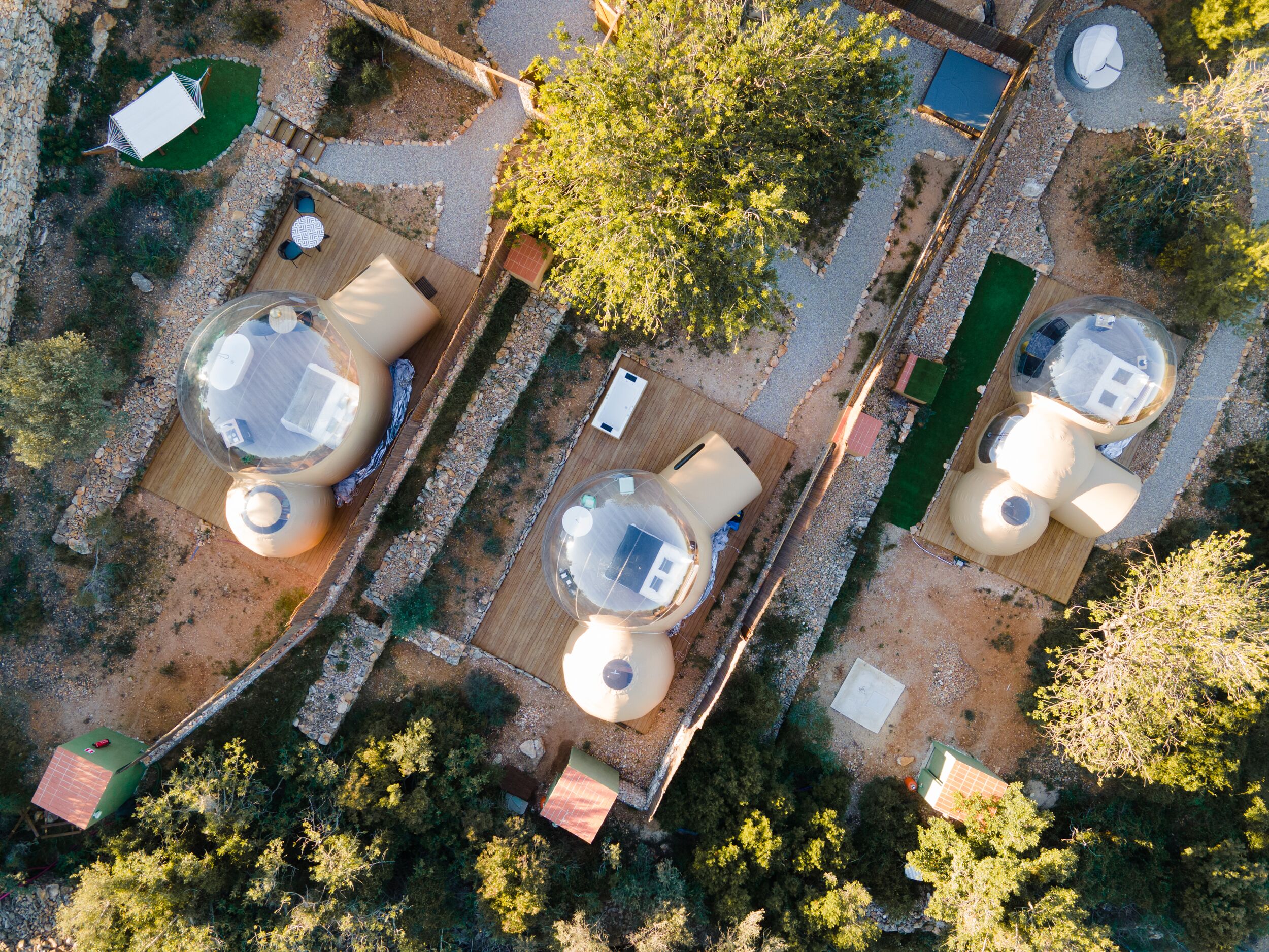 Vista aérea de un complejo turístico con varias habitaciones esféricas, un sendero central y abundante vegetación.