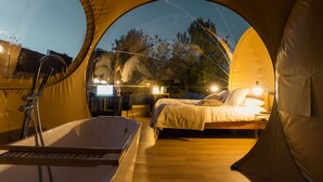 A circular tent-style room with a bed, bedside table, lamp, and a small table with a chair.