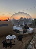 Estrutura em cúpula transparente com cama, área de estar e mesa.